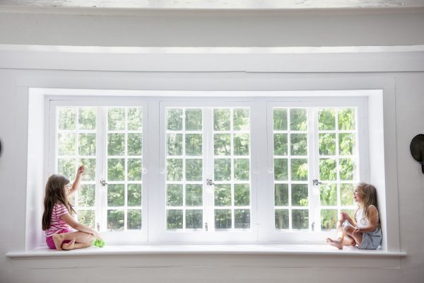 Two girls playing, sitting on a ledge by a large window.