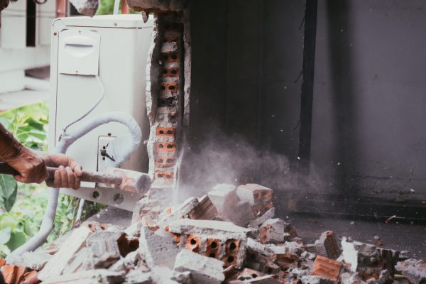 Unrecognizable builder using a sledgehammer breaking and smashing the wall fallen into debris - breaking wall and challenges concept